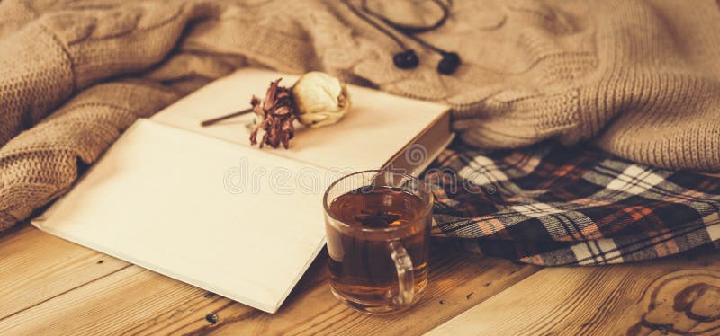 Fall background. Autumn composition with hot tea, book, dry rose flower and knitted sweater. A cup of hot tea, knitted scarf on wooden table. Autumn reading list. Weekend leisure at fall season. Fall background. Autumn composition with hot tea, book, dry rose flower and knitted sweater. A cup of hot tea, knitted scarf on wooden table. Autumn reading list. Weekend leisure at fall season