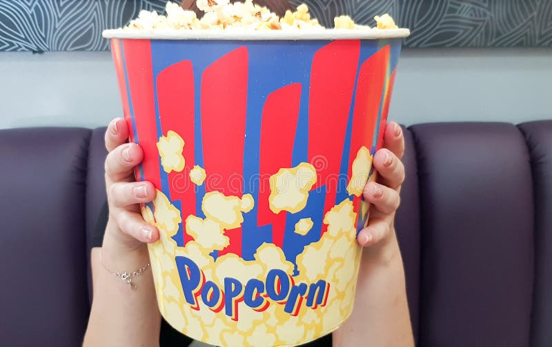 Ucrânia, Kiev - 10 de setembro de 2019: uma garota de cinema segura um grande balde de pipoca em suas mãos, um conceito de assist fotos de stock royalty free Ucrânia, Kiev - 10 de setembro de 2019: uma garota de cinema segura um grande balde de pipoca em suas mãos, um conceito de assist fotos de stock royalty free