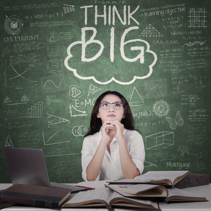 Beautiful female high school student sitting in the classroom with books on the table and text of Think Big on the blackboard. Beautiful female high school student sitting in the classroom with books on the table and text of Think Big on the blackboard