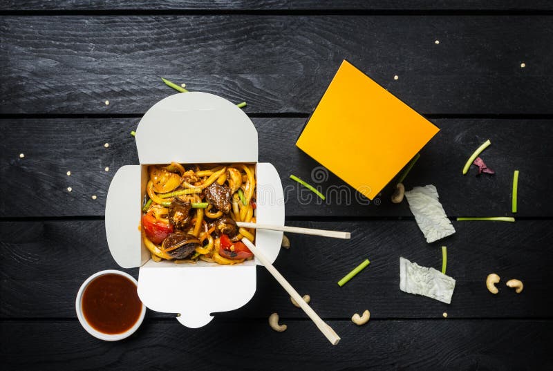 Udon stir fry noodles with meat or chicken in a box. Black background. With chopsticks and sauce.