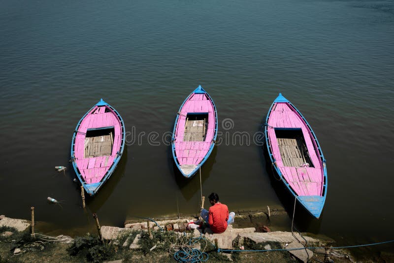 Am Ufer des Ganges werden drei rosa und blaue Holzboote festgemacht. lizenzfreie stockbilder