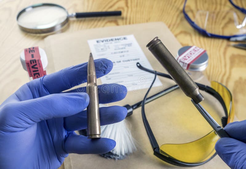 Ufficiale di polizia esperto che confronta due pallottole nel laboratorio di balistica fotografie stock Ufficiale di polizia esperto che confronta due pallottole nel laboratorio di balistica fotografie stock