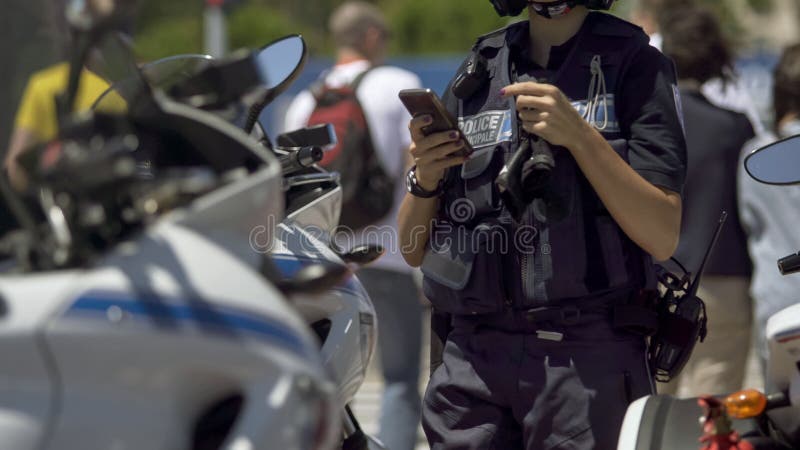 Ufficiale di polizia femminile che sta accanto alla motocicletta, controllante telefono cellulare in servizio