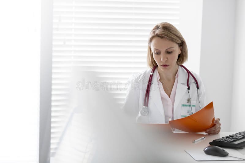Ufna dojrzała doktorska czytanie kartoteka przy biurkiem w szpitalu fotografia stock Ufna dojrzała doktorska czytanie kartoteka przy biurkiem w szpitalu fotografia stock