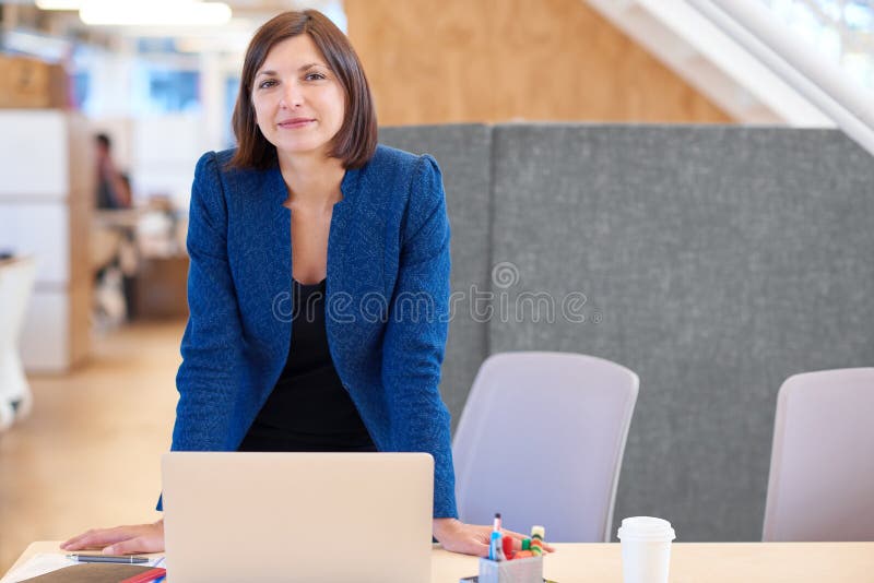 Ufny bizneswoman ono uśmiecha się podczas gdy stojący przy jej biurkiem zdjęcie stock Ufny bizneswoman ono uśmiecha się podczas gdy stojący przy jej biurkiem zdjęcie stock