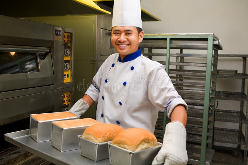 Male baker smiling while holding fresh bread from oven. Male baker smiling while holding fresh bread from oven