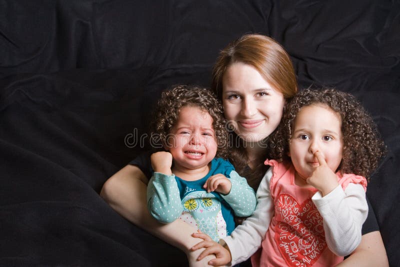 Single mother holding her toddlers in her lap, one toddler is having a temper tantrum and the other toddler is picking her nose. Single mother holding her toddlers in her lap, one toddler is having a temper tantrum and the other toddler is picking her nose