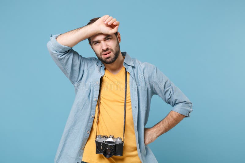 Exhausted traveler tourist man in yellow summer casual clothes with photo camera isolated on blue background. Male passenger traveling abroad on weekends. Air flight journey concept. Put hand on head. Exhausted traveler tourist man in yellow summer casual clothes with photo camera isolated on blue background. Male passenger traveling abroad on weekends. Air flight journey concept. Put hand on head