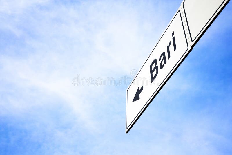 White signboard with an arrow pointing left towards Bari, Apulia, Italy, against a hazy blue sky in a concept of travel, navigation and direction. Path included for the signboard. White signboard with an arrow pointing left towards Bari, Apulia, Italy, against a hazy blue sky in a concept of travel, navigation and direction. Path included for the signboard