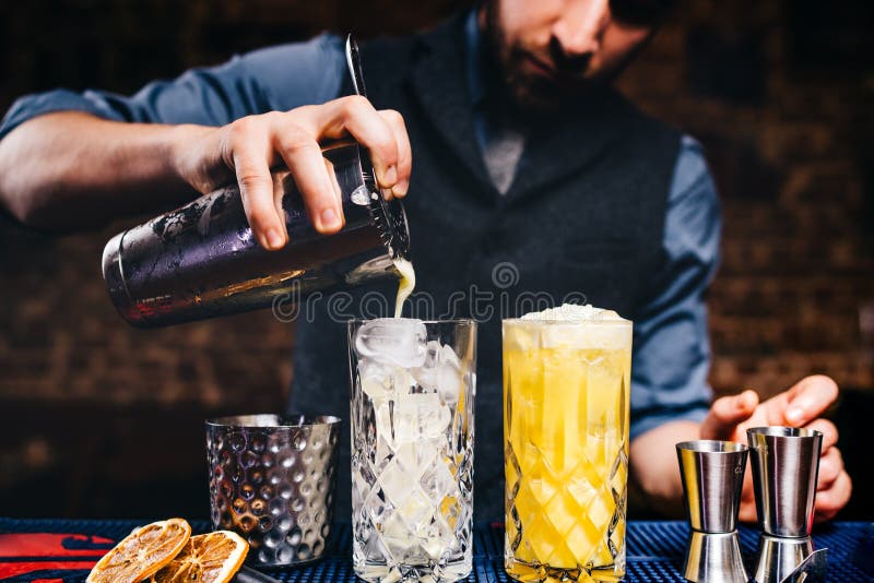 Uitstekende barman die verse oranje wodkacocktail over ijs in kristalglaswerk gieten royalty-vrije stock foto Uitstekende barman die verse oranje wodkacocktail over ijs in kristalglaswerk gieten royalty-vrije stock foto