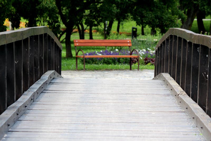 Uitstekende retro romantische oude houten brug die naar houten openbare die parkbank leiden met metaalsteun met bloemen wordt omr stock foto Uitstekende retro romantische oude houten brug die naar houten openbare die parkbank leiden met metaalsteun met bloemen wordt omr stock foto