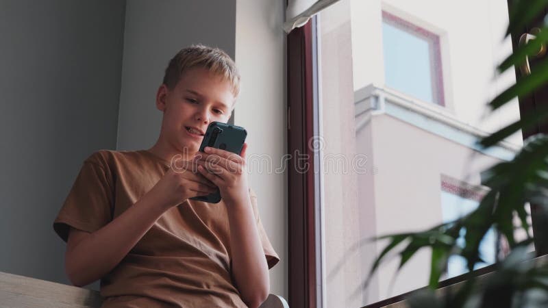 retrato cenimatic menino jogando no celular enquanto espera por comida,  garoto sentado no café enviando texto para amigos, criança jogando jogo  online no telefone. 9711757 Foto de stock no Vecteezy