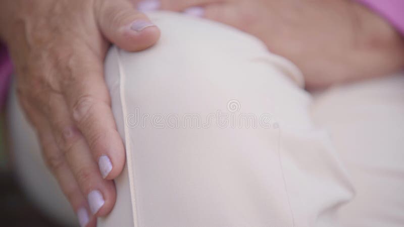 Um aperto extremo da mão feminina madura com manicure suave acariciando o joelho Mulher caucasiana sênior sofrendo de