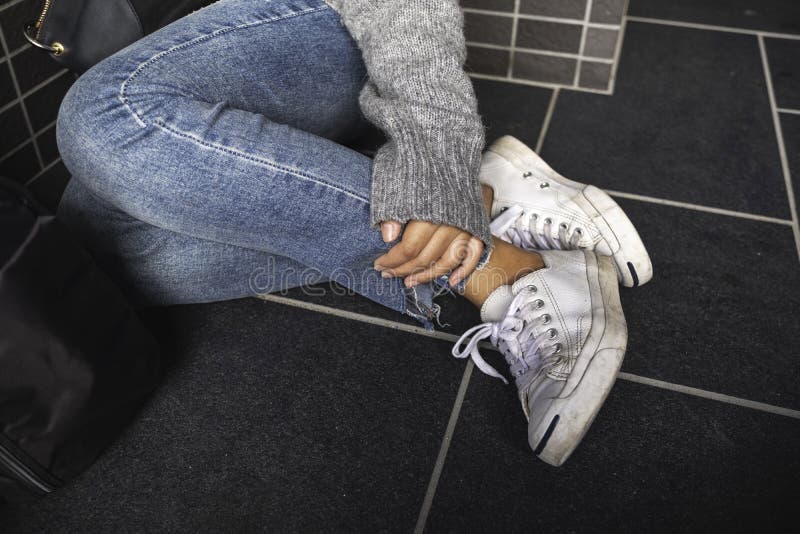 Um brim vestindo da mulher e umas sapatilhas brancas que tocam em seu pé ao sentar-se no assoalho fotos de stock Um brim vestindo da mulher e umas sapatilhas brancas que tocam em seu pé ao sentar-se no assoalho fotos de stock