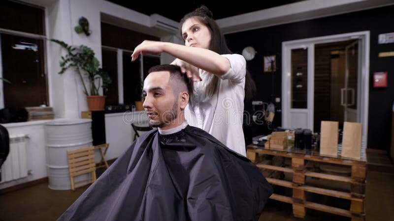 Um cabeleireiro da mulher termina o cabelo que denomina para um visitante de um barbeiro, usos de um cabeleireiro um gel para que