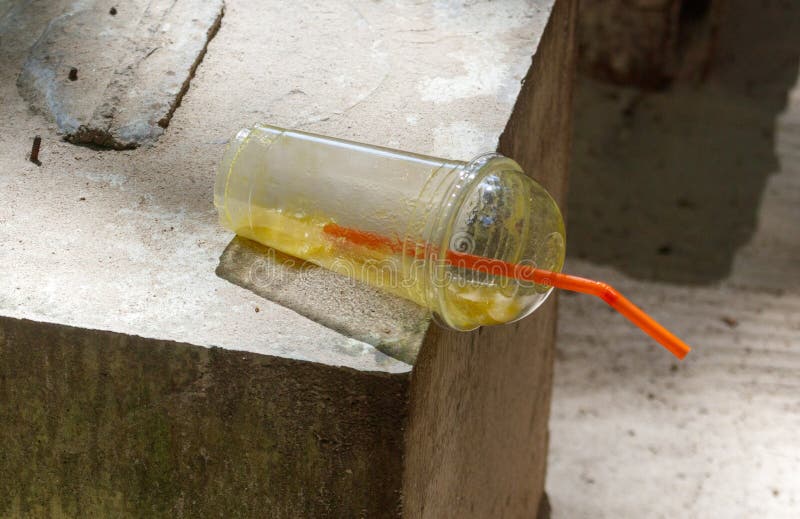 Um copo de plástico com um canudo está sobre um bloco de cimento foto de stock