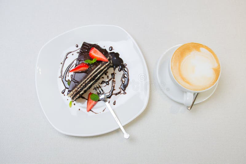 Um copo do café do cappuccino com fatia de bolo de chocolate com morango foto de stock Um copo do café do cappuccino com fatia de bolo de chocolate com morango foto de stock