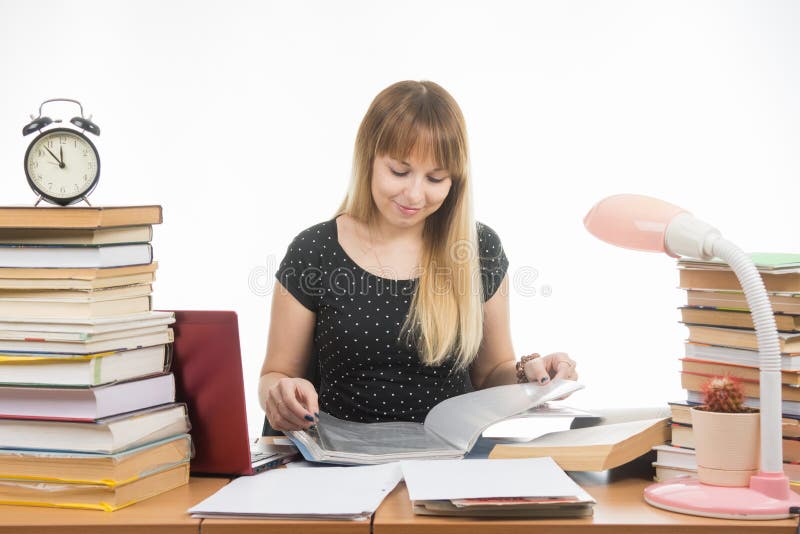 Um estudante em uma tabela desarrumou com os livros na biblioteca com um sorriso, girando as páginas em um dobrador imagem de stock royalty free Um estudante em uma tabela desarrumou com os livros na biblioteca com um sorriso, girando as páginas em um dobrador imagem de stock royalty free