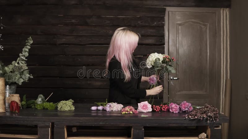 Um florista bonito da menina em um fundo escuro faz uma composição das flores Interior moderno, de madeira filme Um florista bonito da menina em um fundo escuro faz uma composição das flores Interior moderno, de madeira filme