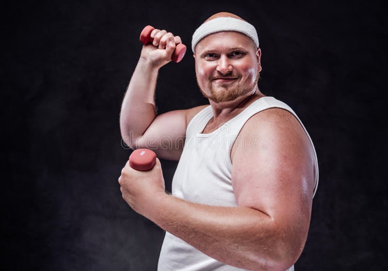 Chubby man with a red face and a white bandage on his head lifts two red dumbbells and looks at the camera smiling. Chubby man with a red face and a white bandage on his head lifts two red dumbbells and looks at the camera smiling