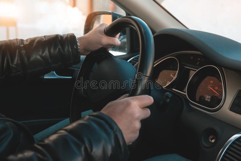 Um grande homem em um casaco de cabedal e em calças de brim senta-se atrás da roda de um carro fotos de stock Um grande homem em um casaco de cabedal e em calças de brim senta-se atrás da roda de um carro fotos de stock
