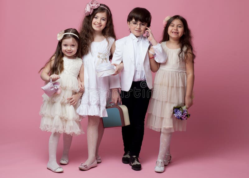 Um grupo de crianças felizes vestidas na roupa clássica bonita do vintage, isolada no fundo cor-de-rosa fotografia de stock Um grupo de crianças felizes vestidas na roupa clássica bonita do vintage, isolada no fundo cor-de-rosa fotografia de stock