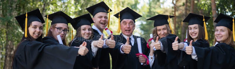 A group of graduates in robes give a thumbs up outdoors. Elderly student. Widescreen. A group of graduates in robes give a thumbs up outdoors. Elderly student. Widescreen