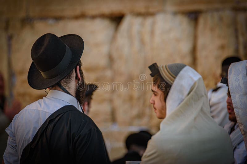 A diverse group of individuals wearing white robes are gathered together looking intently at a wall. A diverse group of individuals wearing white robes are gathered together looking intently at a wall