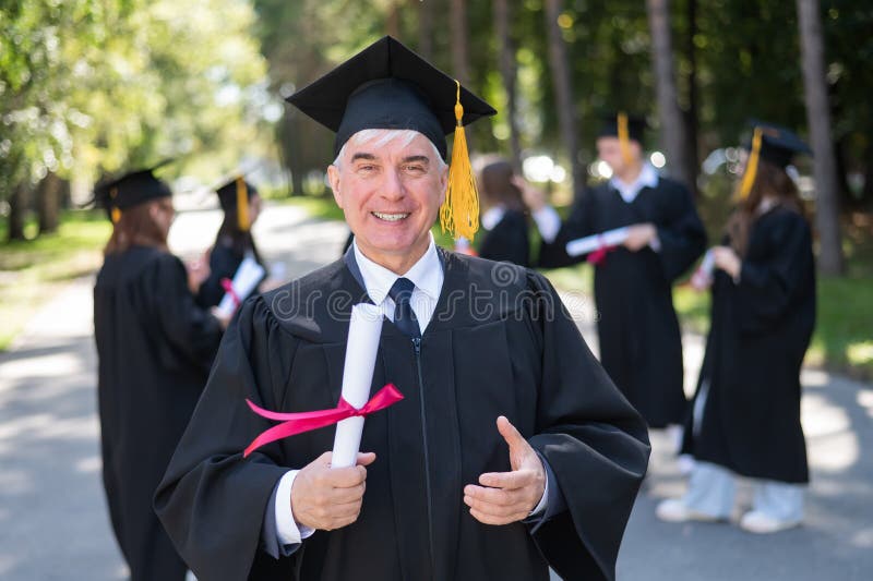 A group of graduates in robes outdoors. An elderly student rejoices at receiving a diploma. A group of graduates in robes outdoors. An elderly student rejoices at receiving a diploma