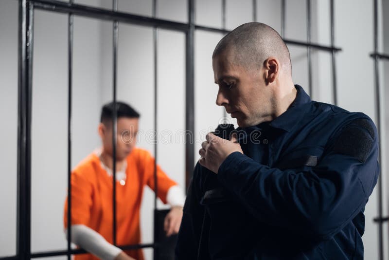 Um guarda prisional com munições completas comunica com o seu parceiro na rádio. no fundo, um prisioneiro numa cela