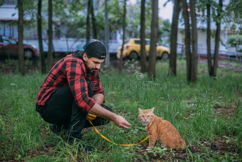 Um homem caminha no parque com seu gato em um arnês