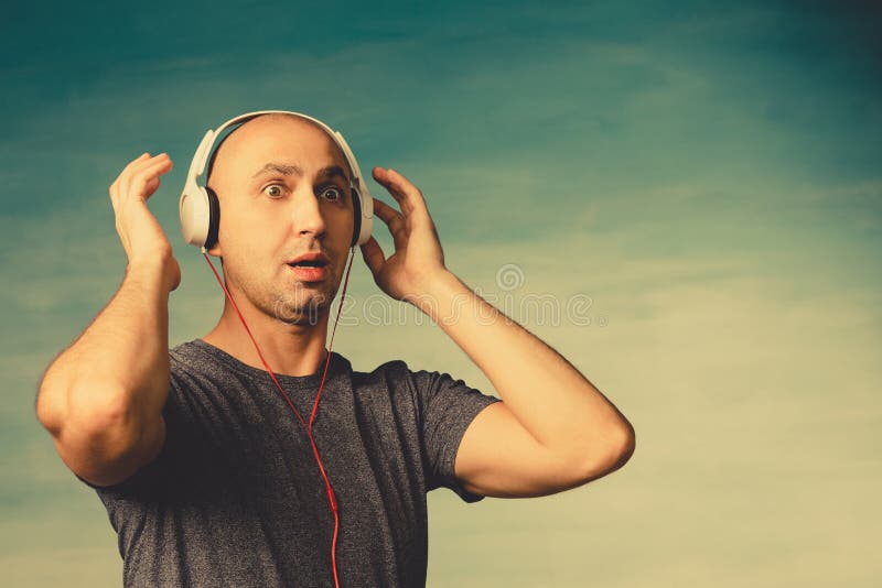 A bald man listens  music in large headphones, Looks in surprise  on a  greenish background. A bald man listens  music in large headphones, Looks in surprise  on a  greenish background.