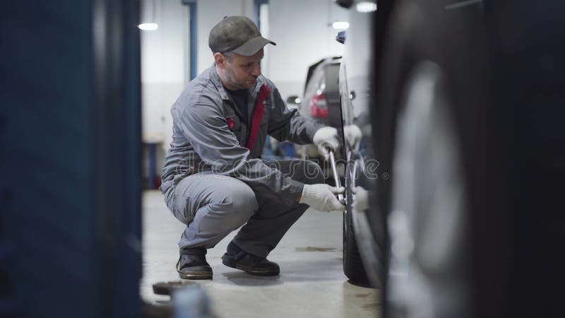 Um homem caucasiano adulto de longa data apertando parafusos na roda do carro. retrato lateral do engenheiro de manutenção em vest