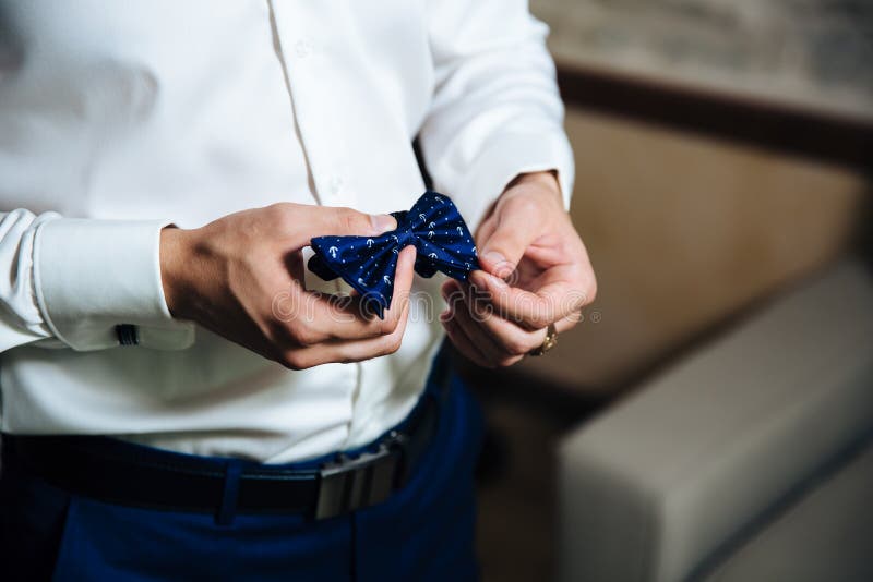 Um homem em um terno de negócio, em uma camisa branca com a grande e calças à moda escura, guarda um laço azul em sua mão A foto de stock royalty free Um homem em um terno de negócio, em uma camisa branca com a grande e calças à moda escura, guarda um laço azul em sua mão A foto de stock royalty free