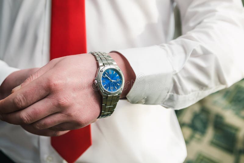 Um homem em uma camisa branca e em um laço vermelho põe um relógio de pulso sobre seu braço fotos de stock Um homem em uma camisa branca e em um laço vermelho põe um relógio de pulso sobre seu braço fotos de stock