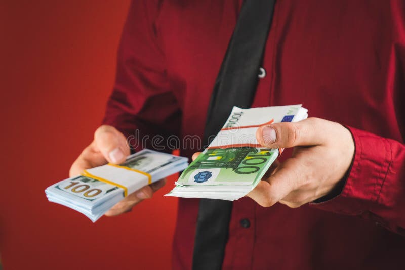 um homem em uma camisa vermelha com um cart?o realiza em sua m?o um punhado das contas em um fundo vermelho foto de stock um homem em uma camisa vermelha com um cart?o realiza em sua m?o um punhado das contas em um fundo vermelho foto de stock