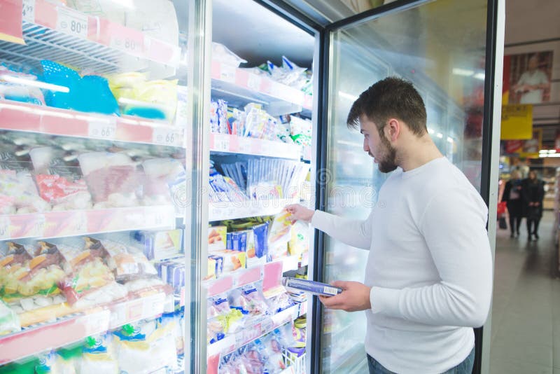 Um homem escolhe alimentos congelados das prateleiras em um refrigerador em um supermercado Um homem compra produtos na loja