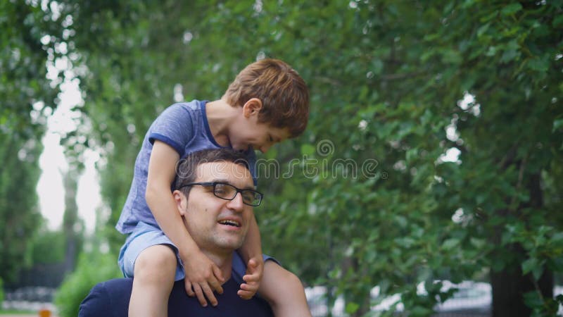 Um homem feliz e adulto leva seu filho pequeno em seus ombros, um menino gosta de passar seus dias livres do verão em um ` s dos