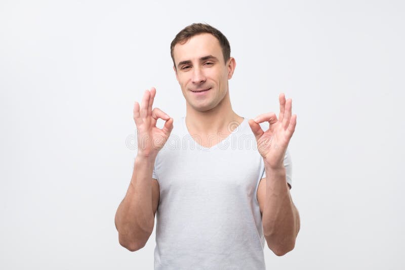 Um homem italiano novo considerável no sinal cinzento da aprovação da exibição do t-shirt imagem de stock royalty free Um homem italiano novo considerável no sinal cinzento da aprovação da exibição do t-shirt imagem de stock royalty free