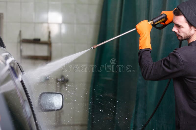Um homem lava um carro com uma mangueira de borracha fotos de stock Um homem lava um carro com uma mangueira de borracha fotos de stock