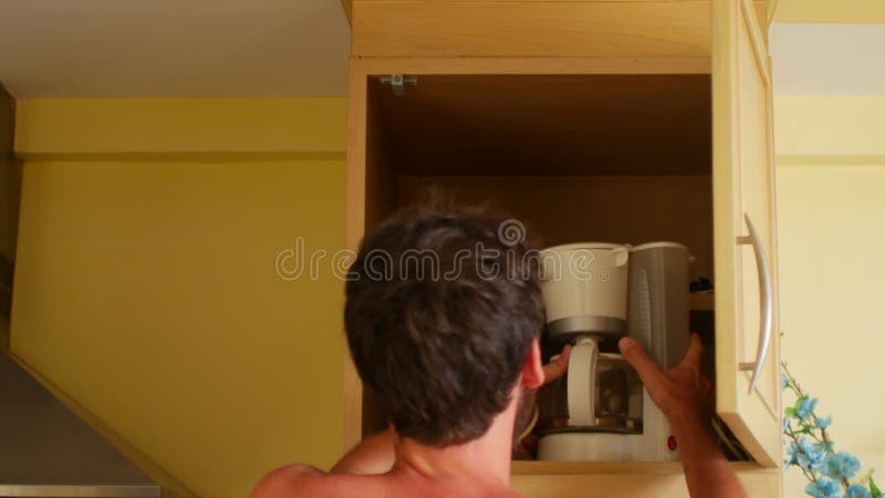 Um homem leva um cafeeiro da prateleira da cozinha