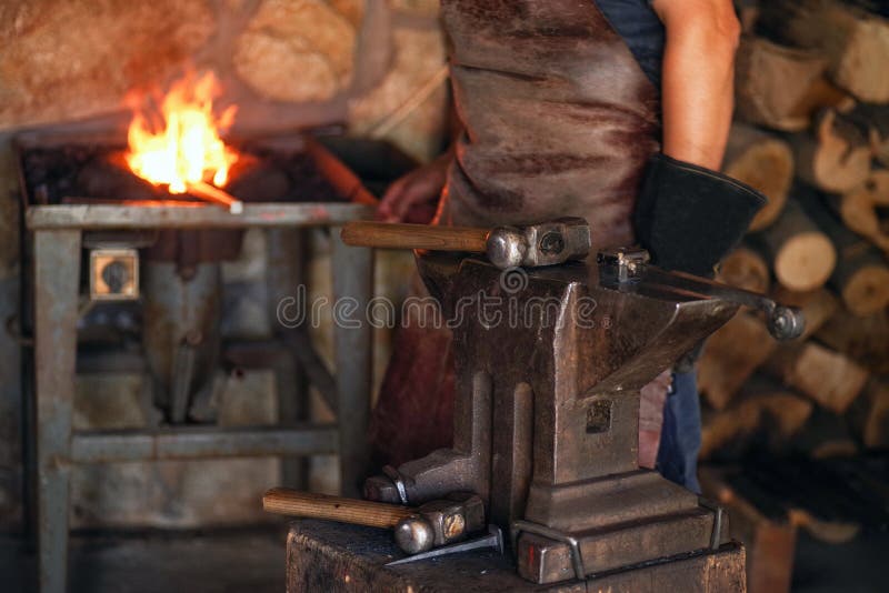 Um homem na roupa de trabalho trabalha com metal Um homem guarda um martelo e um metal quente em sua mão imagens de stock royalty free Um homem na roupa de trabalho trabalha com metal Um homem guarda um martelo e um metal quente em sua mão imagens de stock royalty free