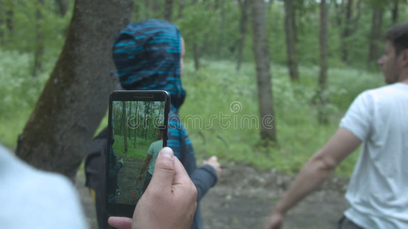 Um homem novo de caminhada em um t-shirt branco e em uma jovem mulher através de uma tela do smartphone Através do telefone um ho