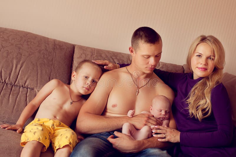 Um homem novo forte senta-se com suas crianças e esposa em casa no th fotografia de stock royalty free Um homem novo forte senta-se com suas crianças e esposa em casa no th fotografia de stock royalty free