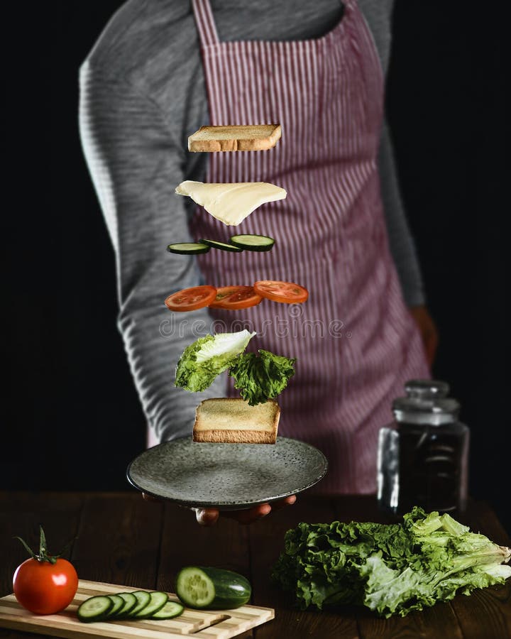 Um homem prepara os ingredientes para um sanduíche delicioso do vegetariano foto de stock Um homem prepara os ingredientes para um sanduíche delicioso do vegetariano foto de stock