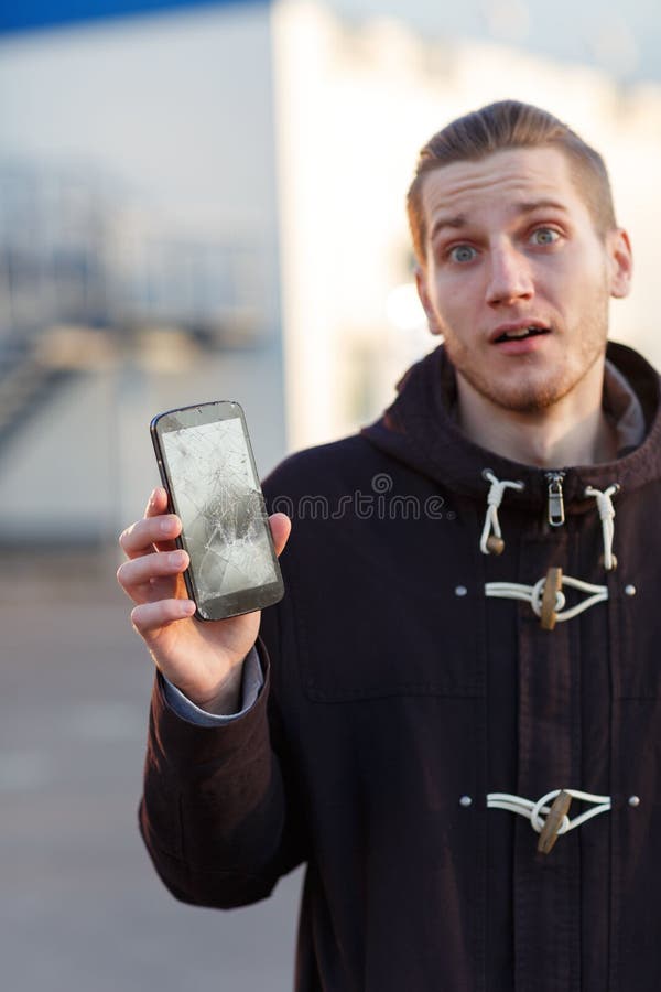 Um indivíduo novo que está na rua está guardando um smartphone quebrado e é insultado foto de stock royalty free Um indivíduo novo que está na rua está guardando um smartphone quebrado e é insultado foto de stock royalty free