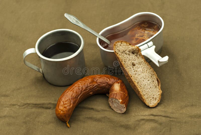 A scanty road meal: soup in a mess tin, coffee in a vintage army mug, a loaf of bread and a piece of sausage on a spread tarpaulin. A scanty road meal: soup in a mess tin, coffee in a vintage army mug, a loaf of bread and a piece of sausage on a spread tarpaulin