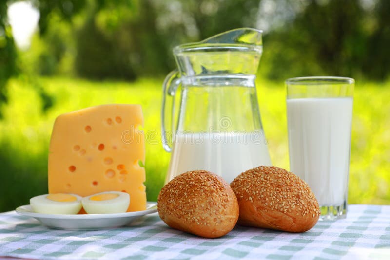 Um jarro de leite, um vidro do leite, uma parte de queijo e um ovo cortado em uma placa fotos de stock Um jarro de leite, um vidro do leite, uma parte de queijo e um ovo cortado em uma placa fotos de stock