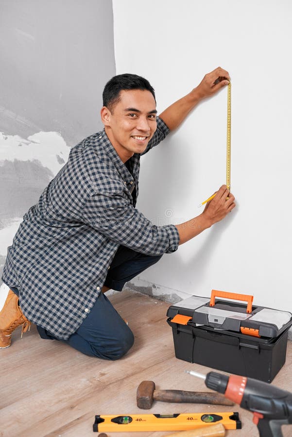 A young Asian man looks at the camera while measuring vertically for home DIY. High quality photo. A young Asian man looks at the camera while measuring vertically for home DIY. High quality photo