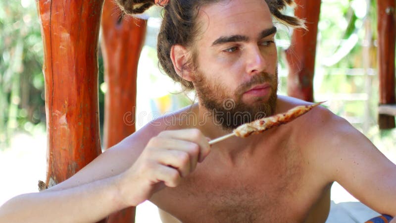 Um jovem com cadeado e barba come galinha